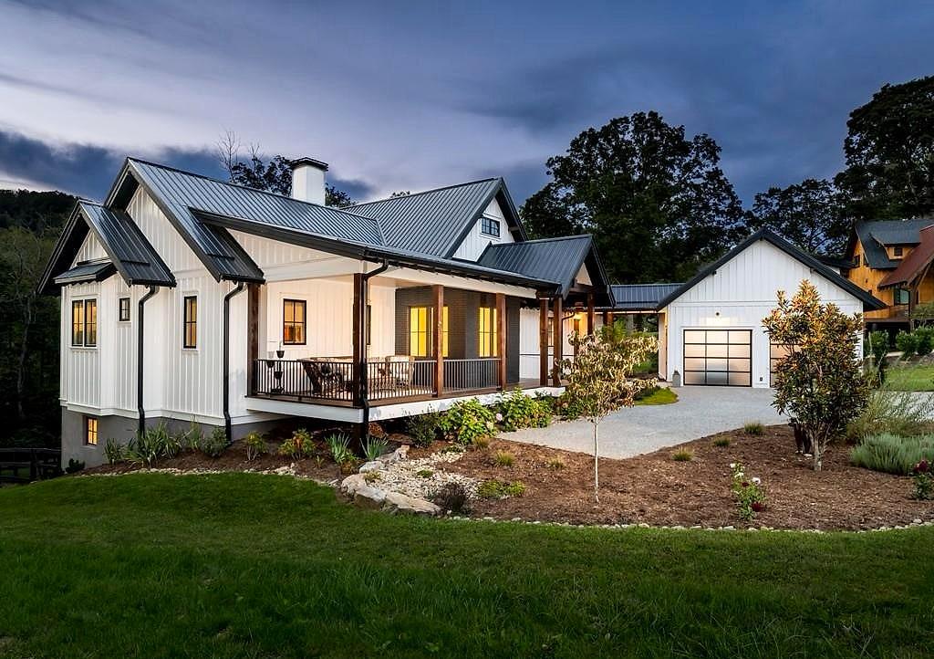 Modern farmhouse at dusk — white board-and-batten, black metal roof and a lit covered porch